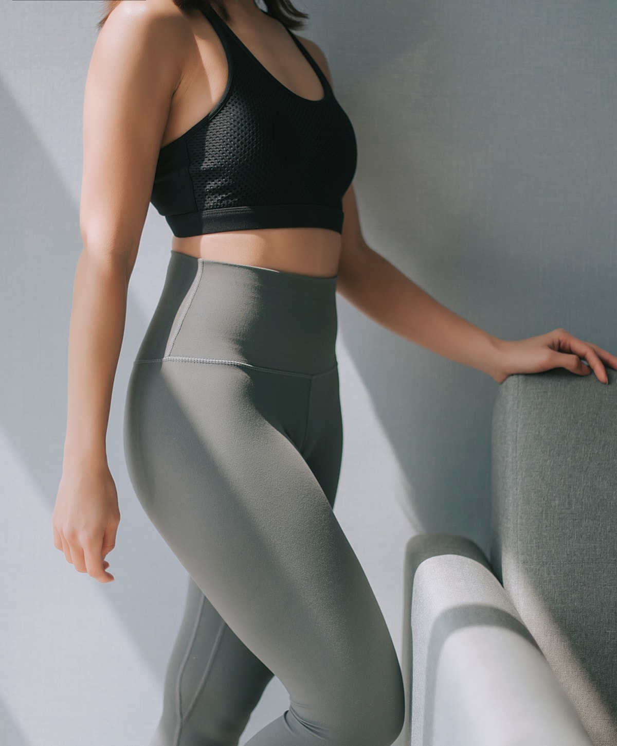 Woman in activewear posing by a sofa.