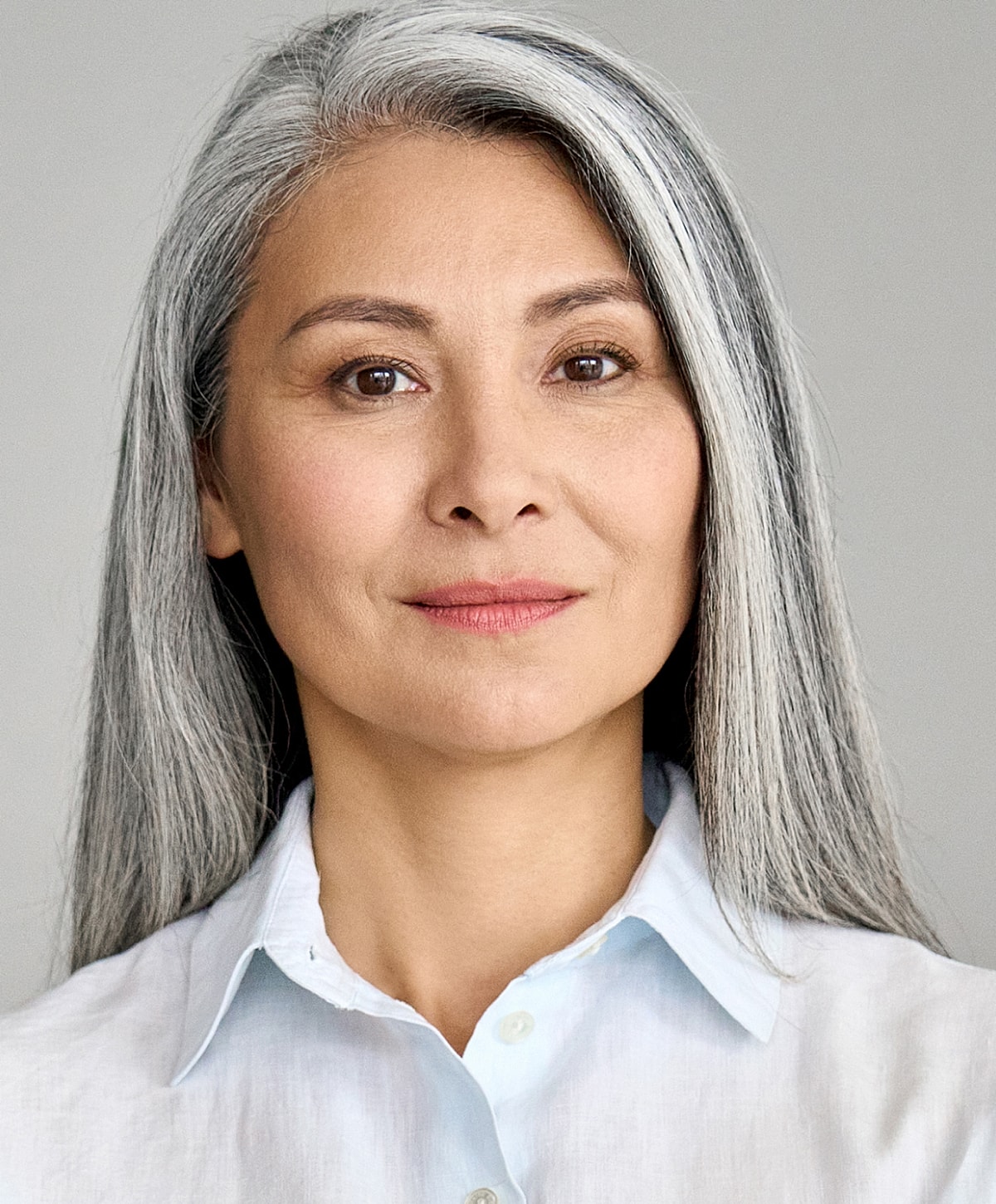 Woman with gray hair gently touching her face.
