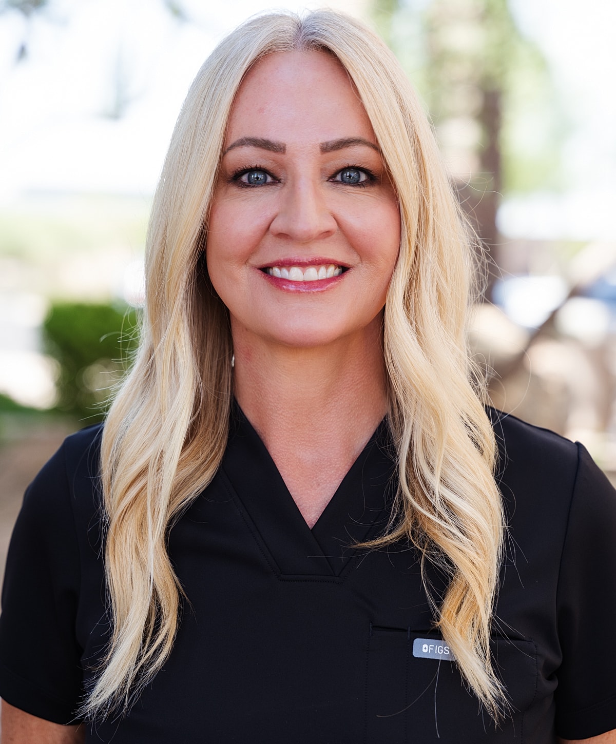 Smiling woman in black scrubs outdoors.
