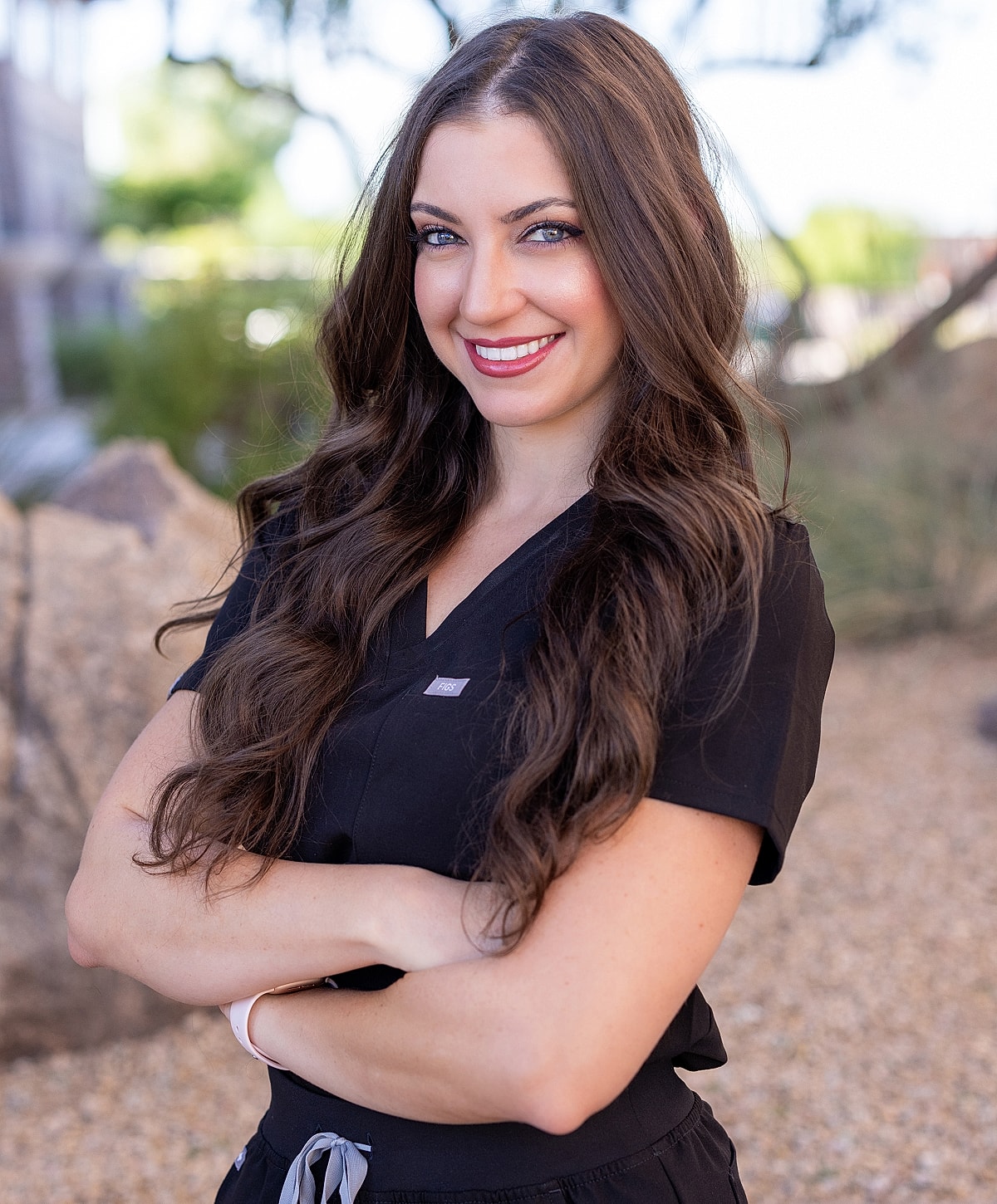 Smiling woman in medical scrubs outdoors.