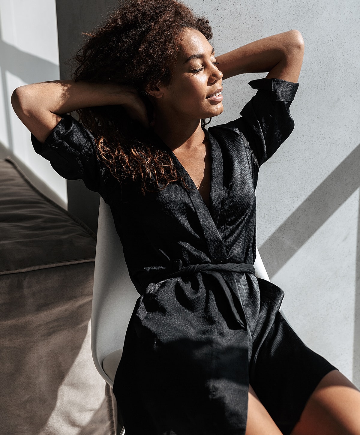 Woman relaxing in black robe, sunlight streaming.