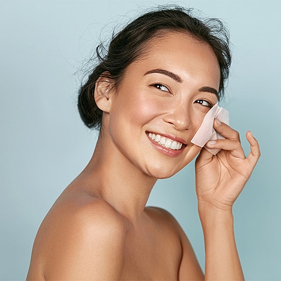 Smiling woman applying skincare on her face.