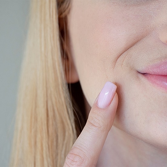 Woman touching her face with a pink nail.