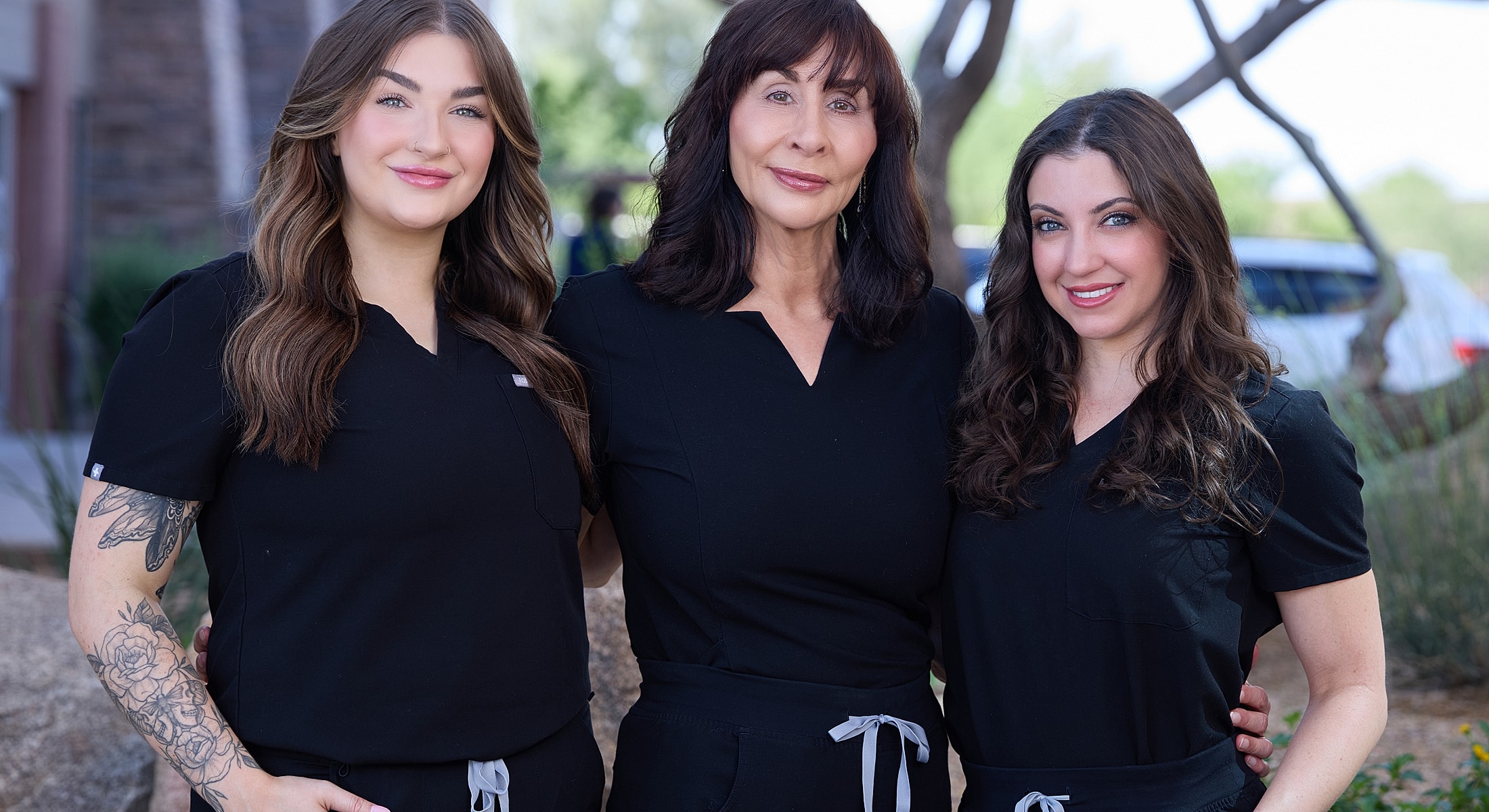 Three women in black scrubs posing outdoors.
